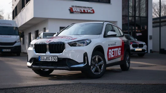 Weißer BMW-SUV mit roter „RETTIG“-Werbung vor einem Autohaus